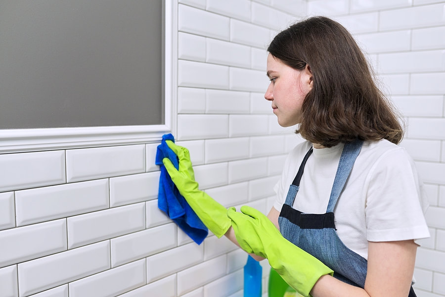 a woman in a white shirt and blue apron cleaning a white tile wallPicture