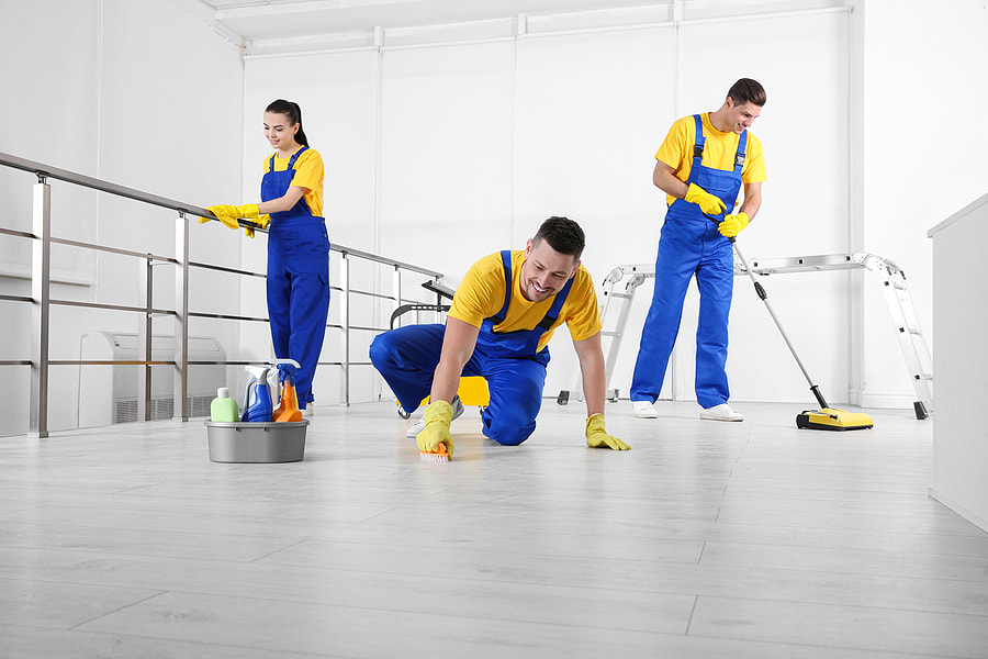 workers in blue overalls and yellow gloves cleaning a floor