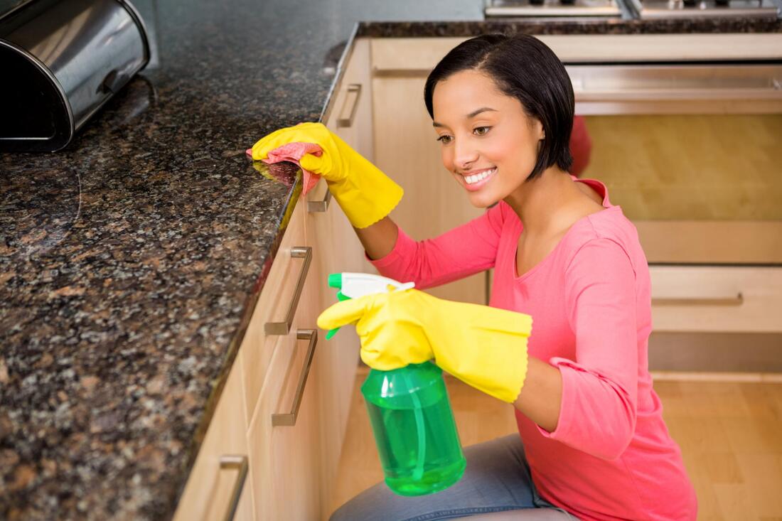 a woman cleaning a kitchen counter with yellow gloves