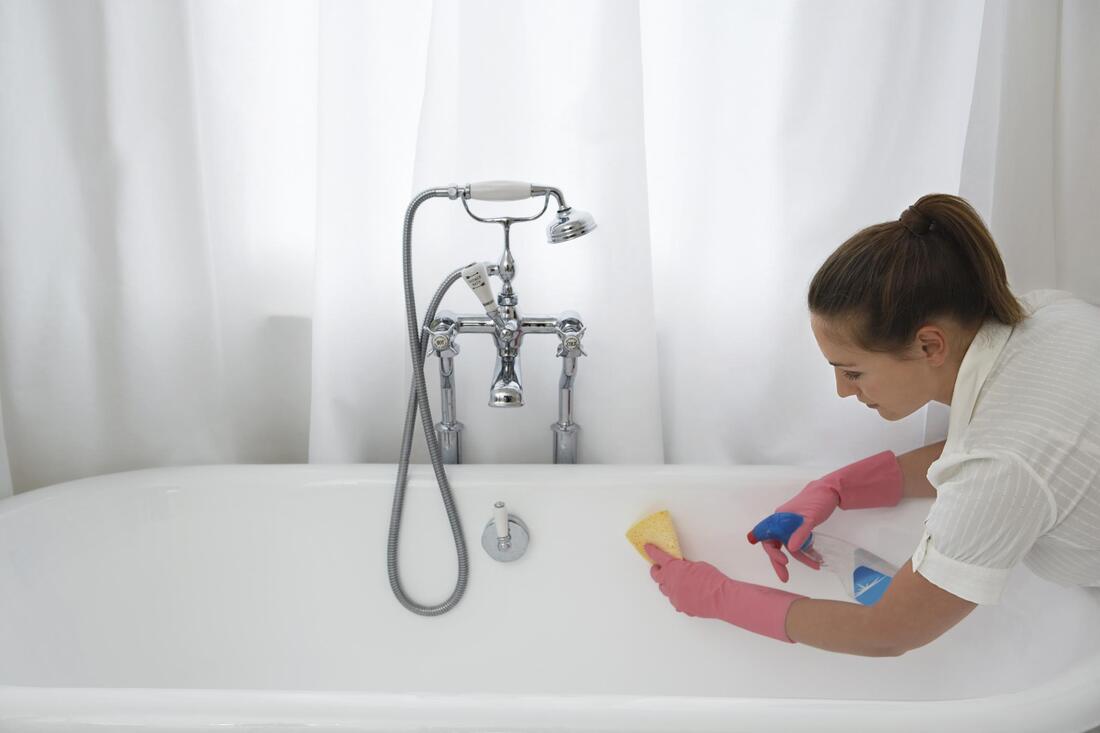 a woman cleaning a bathtub with a sponge